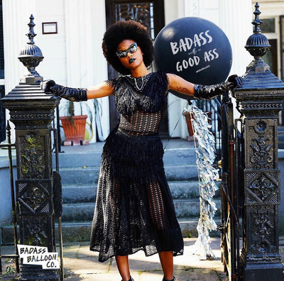 Beautiful model with a badass attitude in front of a giant black balloon that reads in white letters "Baddass With A Good Ass" - by Baddass Balloon Co. 